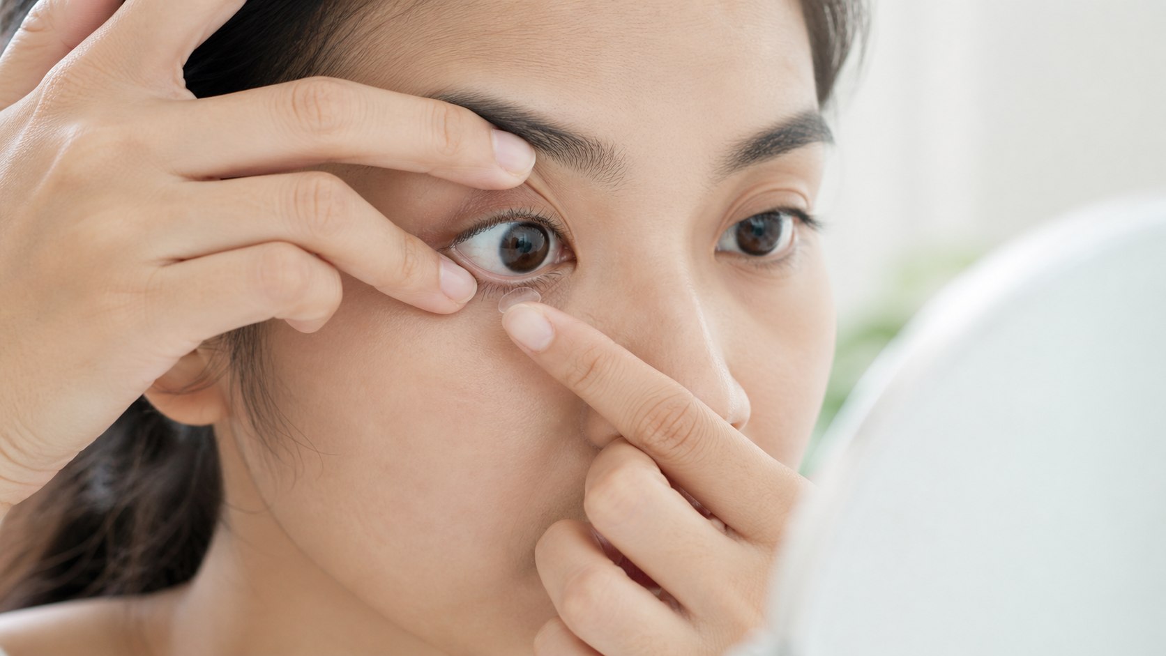 Woman gently inserting a soft contact lens while holding her eyelids open