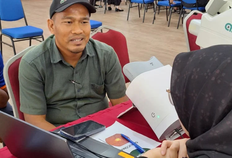 Participant receiving personalised eye consultation from OptiSaver optometrist during CSR event in Malaysia. Optional ca
